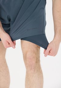 Donkergrijze shorts van glad, lichtgewicht materiaal, met het logo "ENDURANCE" gedrukt nabij de zoom, met een strakke pasvorm en een zijsplit.