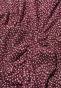 Tissu bourgogne texturé avec des pois blancs. Présente des sections froncées et des plis flottants créant une apparence douce et drapée.