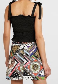 Top corto a sbuffo nero con scollatura arricciata e spalline regolabili, abbinato a una gonna multicolore con motivi geometrici e floreali.