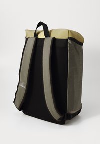 Sac à dos avec un haut jaune, des panneaux latéraux en maille grise et noire, des bretelles ajustables et un logo adidas discret sur le côté.