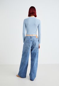 Light blue ribbed long-sleeve top and wide-leg faded blue jeans with back pockets and leather tag, viewed from the back.