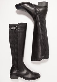 Bottes noires en cuir montantes, avec un panneau texturé, fermeture éclair et un petit talon, dotées de détails de sangle ajustable.