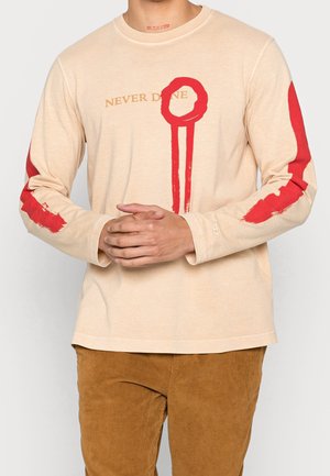 Beige Langarm-T-Shirt mit rotfarbenen, malerischen Akzenten an den Ärmeln, mit dem Text "NEVER DONE" in Gold. Weicher, lässiger Stoff.
