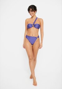Vijoličen bikini komplet, ki vključuje zgornji del z enim naramnicam in zasukano zasnovo ter obročnim poudarkom, v kombinaciji z visokimi hlačkami, oba iz gladkega materiala.