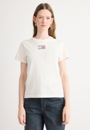 T-shirt a maniche corte e colletto rotondo in cotone avorio con un piccolo design di strass colorati sul davanti, abbinato a jeans blu scuro.