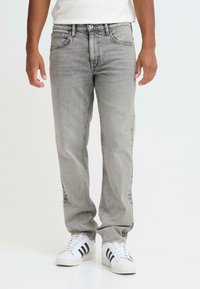 Jean en denim gris avec une coupe droite, doté d'un design classique à cinq poches et de légères zones délavées, associé à des baskets blanches.