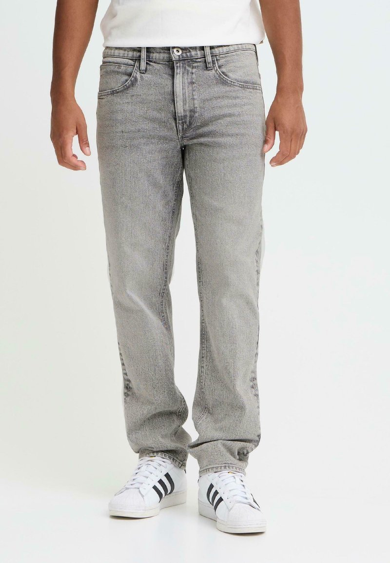 Jean en denim gris avec une coupe droite, doté d'un design classique à cinq poches et de légères zones délavées, associé à des baskets blanches.