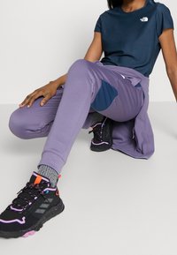 Laivastonsininen pyöreäkauluksinen t-paita, violetit ribbineuloshousut laivastonsinisillä paikoilla ja mustat vaelluskengät, joissa on vaaleanpunaiset yksityiskohdat ja kuvioidut pohjat.