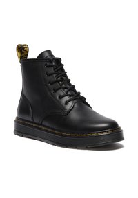 Bottine noire en cuir à lacets avec semelle épaisse à rainures, coutures jaunes et languette en tissu avec logo à l'arrière.