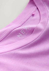 Hellrosa T-Shirt mit kurzen Ärmeln aus weichem Baumwollstoff, mit rundem Ausschnitt und sichtbar angebrachtem Etikett im Kragen. Glatte Textur.