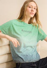 Zelené gradientové tričko s texturovaným vzorem, na kterém je šedý text "il paradiso". Krátké rukávy, volný střih a měkká látka.