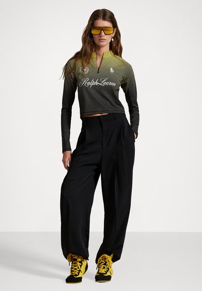 Kuttet svart og gul langermet topp med mesh-design og Ralph Lauren-merke. Løse svarte bukser og sneakers med gule detaljer.