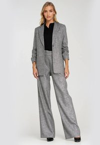 Szary marynarka w kratę i szerokie spodnie w zestawie. Marynarka ma pojedynczy guzik i klapy; materiał ma teksturowane wykończenie. Czarny top pod spodem.