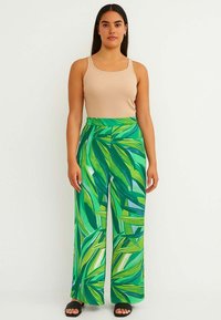 Pantaloni a gamba larga di un verde vivace con stampa fogliosa, realizzati in tessuto leggero. Abbinati a una canotta beige e sandali neri.