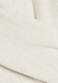 Tissu blanc texturé avec de petites perforations plié délicatement, montrant des détails fins et un motif de surface lisse.