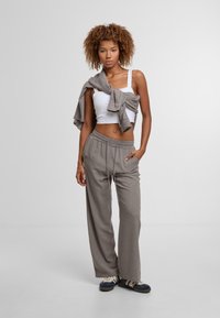 Lichtgrijze, elastische broek met zijzakken en een comfortabele pasvorm, gecombineerd met een wit tanktop en een grijze trui over de schouders draped.