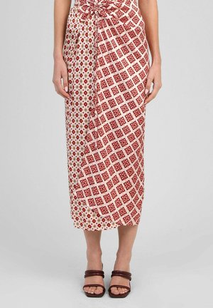 Femme portant une jupe portefeuille midi avec deux motifs rouges différents, floraux et géométriques, associée à des sandales à brides marron foncé.