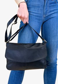 Borsa a tracolla nera in pelle con chiusura a patta e tracolla regolabile, caratterizzata da una texture liscia e dettagli di cucitura minimali.