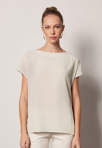 Ljusbeige kortärmad topp med båtutskärning, tillverkad av ett mjukt, något genomskinligt tyg, med en avslappnad passform och enkelt design.