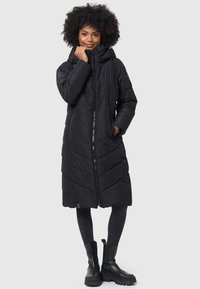 Long manteau noir en doudoune avec fermeture éclair, poches avant et capuche. Présente un design matelassé avec des coutures angulaires pour une texture.
