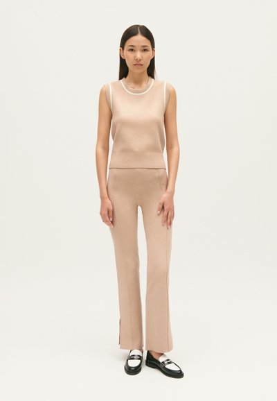 Beige kangast ilma varrukataga top, millel on valge soonikkrae, koos sobivate istuvate pükstega, millel on külgmised lõhud. Mustad ja valged loaferid lõpetavad välja nägemise.