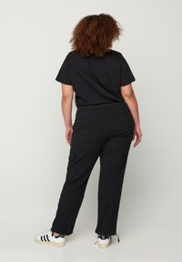 Maglietta nera abbinata a pantaloni cargo neri larghi con tasche e cordini regolabili alla caviglia, indossati con sneakers bianche.