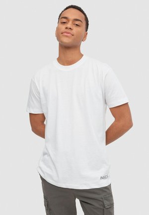 Camiseta de algodón blanca con cuello redondo y mangas cortas. Presenta un pequeño logo "INSIDE" en el lado inferior izquierdo.