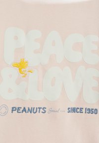 T-shirt di tessuto rosa chiaro con la scritta "PEACE & LOVE" in bianco, caratterizzato da un uccellino cartone animato giallo ricamato e "PEANUTS Social Club" in blu.