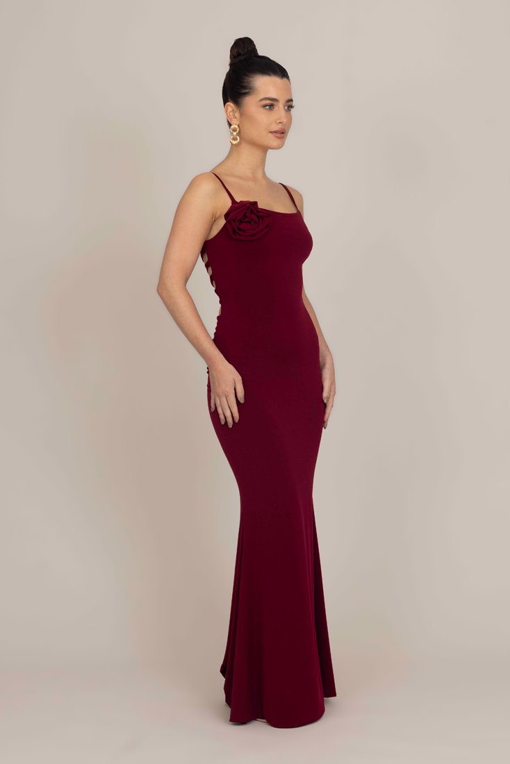 Bordo, uska, bezručna haljina s božurićem sa strane, teksturirana tkanina i lepršavi rub, stvarajući elegantnu siluetu.