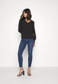 Svart V-halsblus med långa ärmar, matchad med slim fit mörkblå jeans och svarta klackskor med remmar. Slät tygkvalitet, skräddarsydd design.