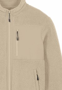 Veste polaire beige avec fermeture éclair intégrale à l'avant, tissu texturé, poche poitrine zippée et poche latérale zippée visible sur le côté droit.