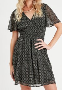 Robe noire à motifs floraux avec des manches courtes et transparentes, une taille cintrée et une jupe évasée. Présente des motifs complexes aux couleurs douces.