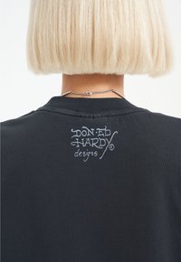 Black t-shirt featuring a white ink logo, "Don Ed Hardy designs," printed at the back, with a smooth texture and classic crew neckline.