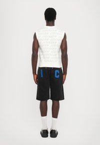 Hvid ærmeløs skjorte med "ICECREAM" gentaget i lys grå, parret med sorte shorts med blå "I" og "C" på baglommene.