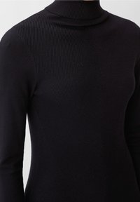 Haut noir en tricot à col montant avec une texture côtelée et un design ajusté, présentant une transition sans couture vers un panneau latéral lisse et moulant.