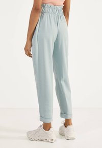 Světlé modré kalhoty s kostkovaným vzorem gingham a stahovací elastickou páskou. Mají zúžené nohavice a vyhrnuté manžety. Nosit s bílými teniskami.