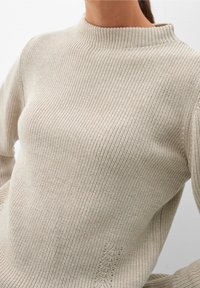 Jasnobeżowy sweter z prążkowanego materiału, z wysokim kołnierzem i długimi rękawami. Posiada subtelny teksturowany wzór oraz lekko dopasowany fason.