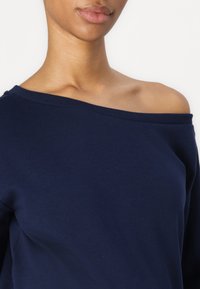 Felpa blu navy off-shoulder con una morbida texture in cotone e collo a coste, caratterizzata da maniche lunghe e un fit rilassato.