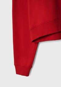 Sweat-shirt rouge à manches longues avec poignets et ceinture côtelés, présenté sur un fond gris clair uni.