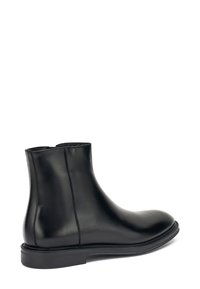 Botines de cuero negro con una textura suave, puntera redondeada y paneles laterales elásticos, que cuentan con una suela plana resistente y un diseño minimalista.