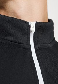 Schwarze Zip-Up-Kollektion Sweatshirt mit einem weißen Reißverschluss, das einen strukturierten Stoff aufweist und eine Nahaufnahme des Kragenbereichs zeigt.