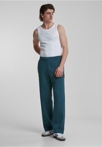 Pantalones de chándal en color verde azulado con una cinturilla ancha y bolsillos laterales, combinados con una camiseta sin mangas blanca. Tela suave, diseño de pierna recta y costuras en contraste.