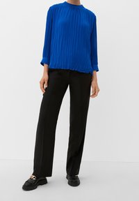 Blusa blu a maniche lunghe plissettata con scollatura rotonda abbinata a pantaloni neri dritti e scarpe nere slip-on con finitura strutturata.