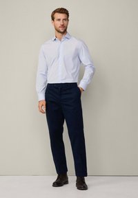 Camicia button-down azzurra chiara, pantaloni blu navy e stivali marroni scuri. Vestibilità slim con maniche lunghe. Tessuto liscio e linee pulite.