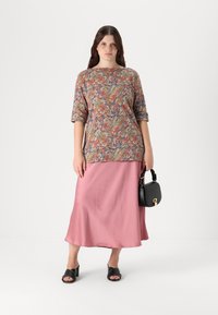 Haut à motif floral dans des tons terreux, associé à une jupe satin rose clair et des sandales à talons blocs noires. Un petit sac à main noir complète le look.