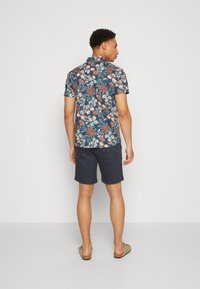 Kortærmet skjorte med blomsterprint i marineblå, med klare blå og jordnære toner. Båret med mørke shorts og casual slip-on sko.