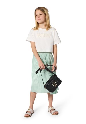 Weißes, kurzes T-Shirt mit „KORS“ in Gold, mintgrüner, plissierter Rock, schwarze, strukturierte Handtasche und weiße Sandalen mit goldenen Akzenten.