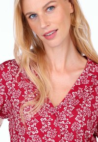 Red floral-patterned dress with a V-neckline, featuring white flowers, short sleeves, and buttons along the front. Smooth fabric texture.