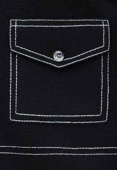 Fekete szövet, varrott mellzsebbel, amelyet fehér cérnaszál körvonalaz és ezüst kapcsos patentzár díszít. Texturált anyag, egyszerű kialakítás.