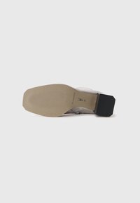Zapato de cuero gris con punta cuadrada, tacón medio y textura suave. La suela es de color marrón claro con un sutil texto y patrones de agarre.